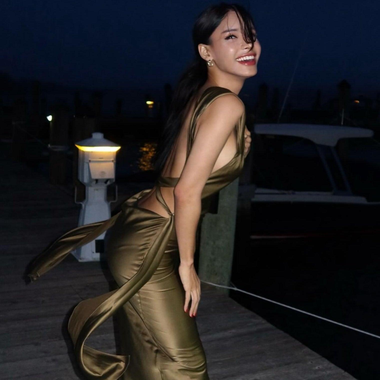 Olive satin maxi dress with a modern slip design, featuring an open back and tied straps, styled for a chic evening look.