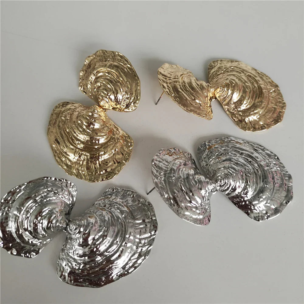 Pair of gold and silver shell-shaped earrings on a gray background