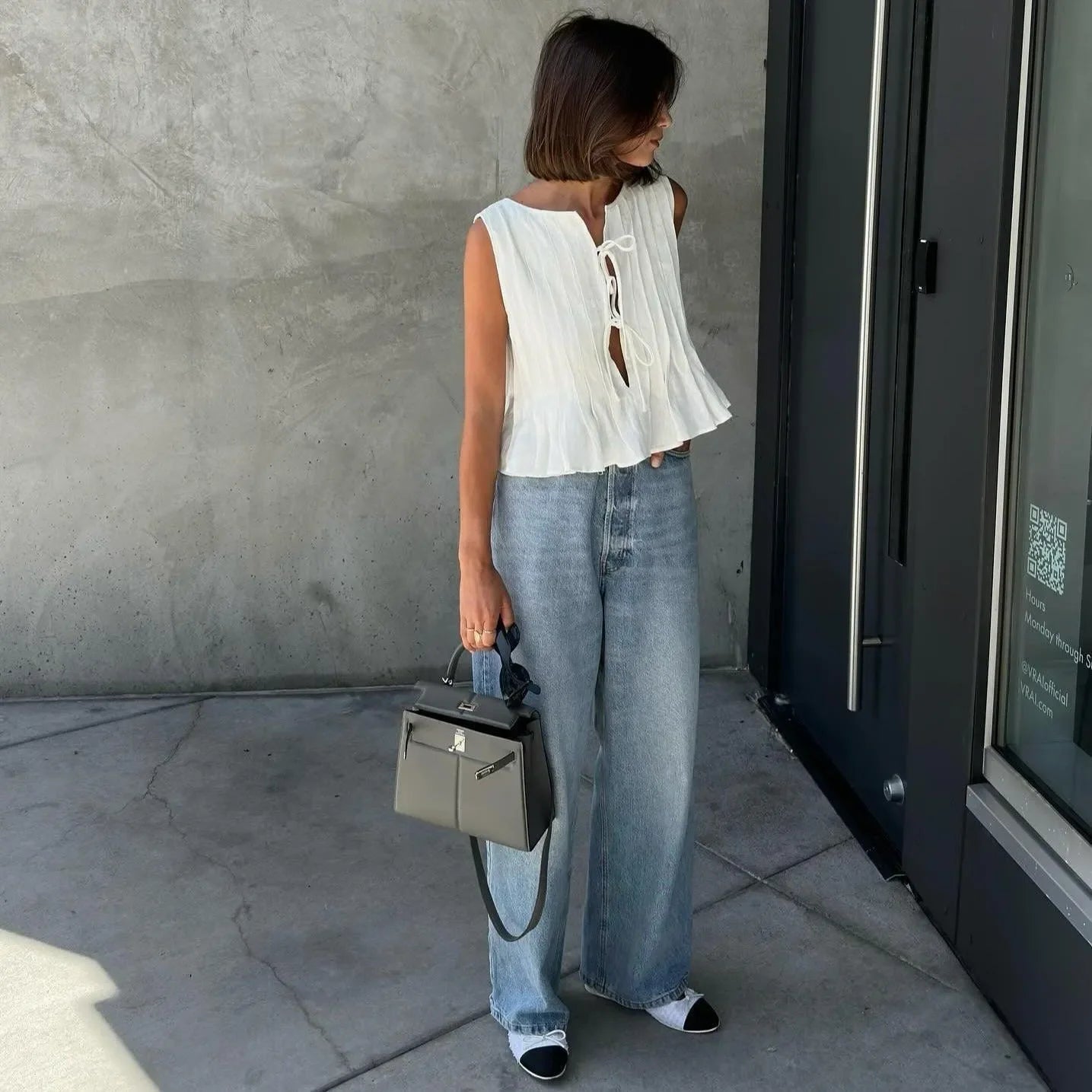 White cotton pleated top with a tie-front detail, styled with wide-leg denim and a chic handbag for a casual look.