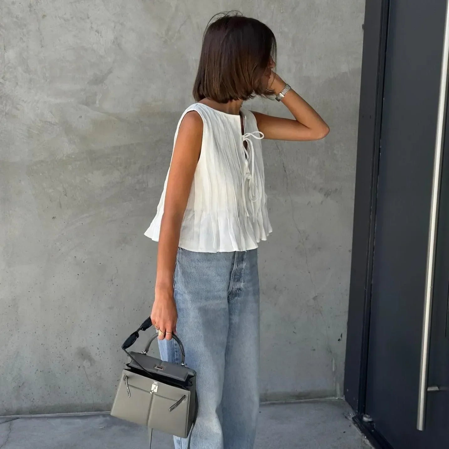 White pleated cotton top with tie detail, styled casually with high-waisted denim and a chic handbag.