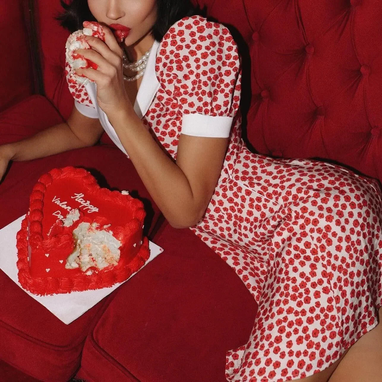 White mini dress with red flower prints, puff sleeves, and a fitted waist, styled with a playful vintage vibe.
