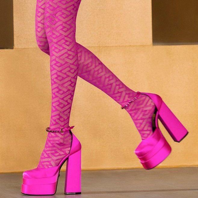Pink platform high heels worn with matching pink tights against a beige background
