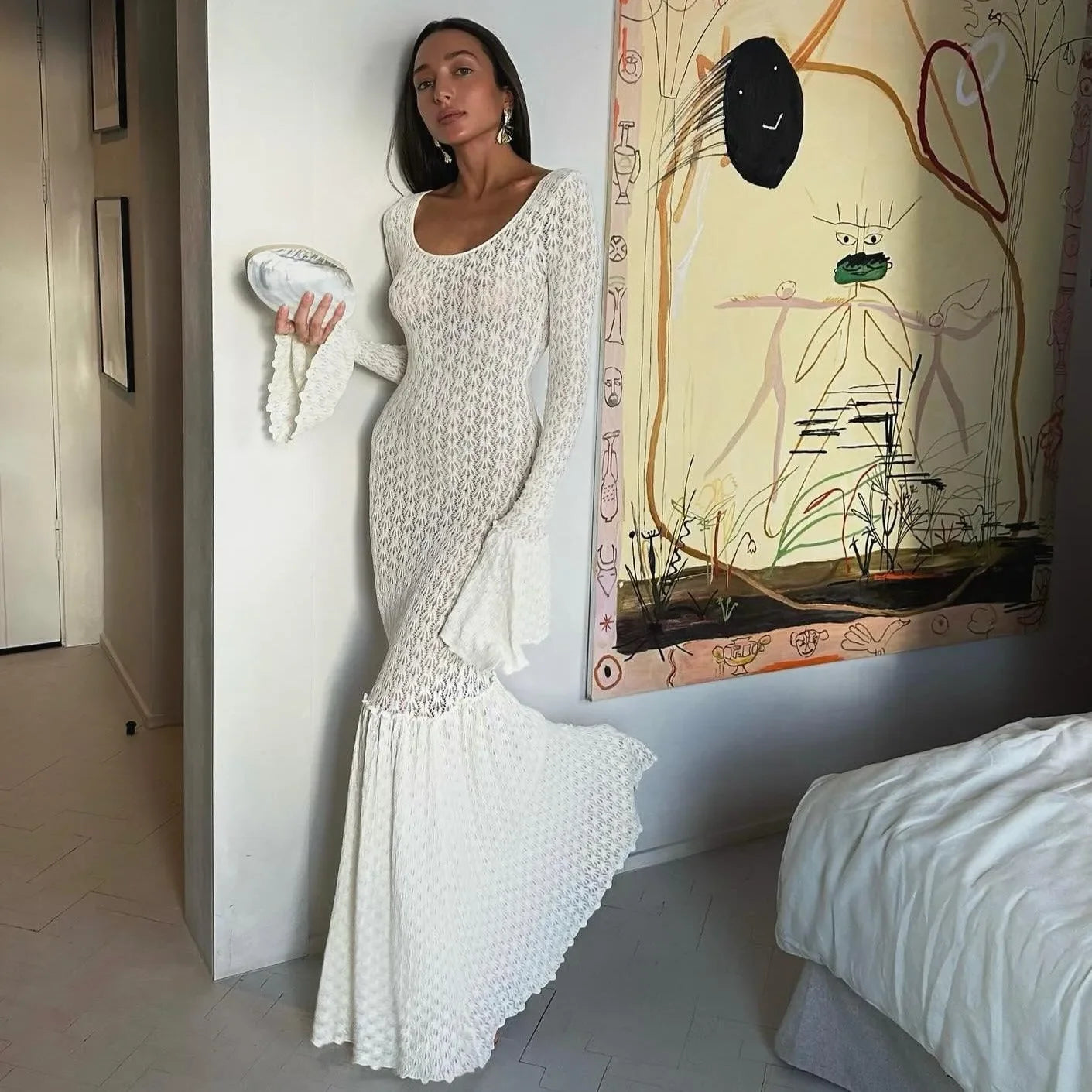 White crochet flare sleeve maxi dress with a fitted bodice, styled elegantly with a clutched bag and statement earrings.