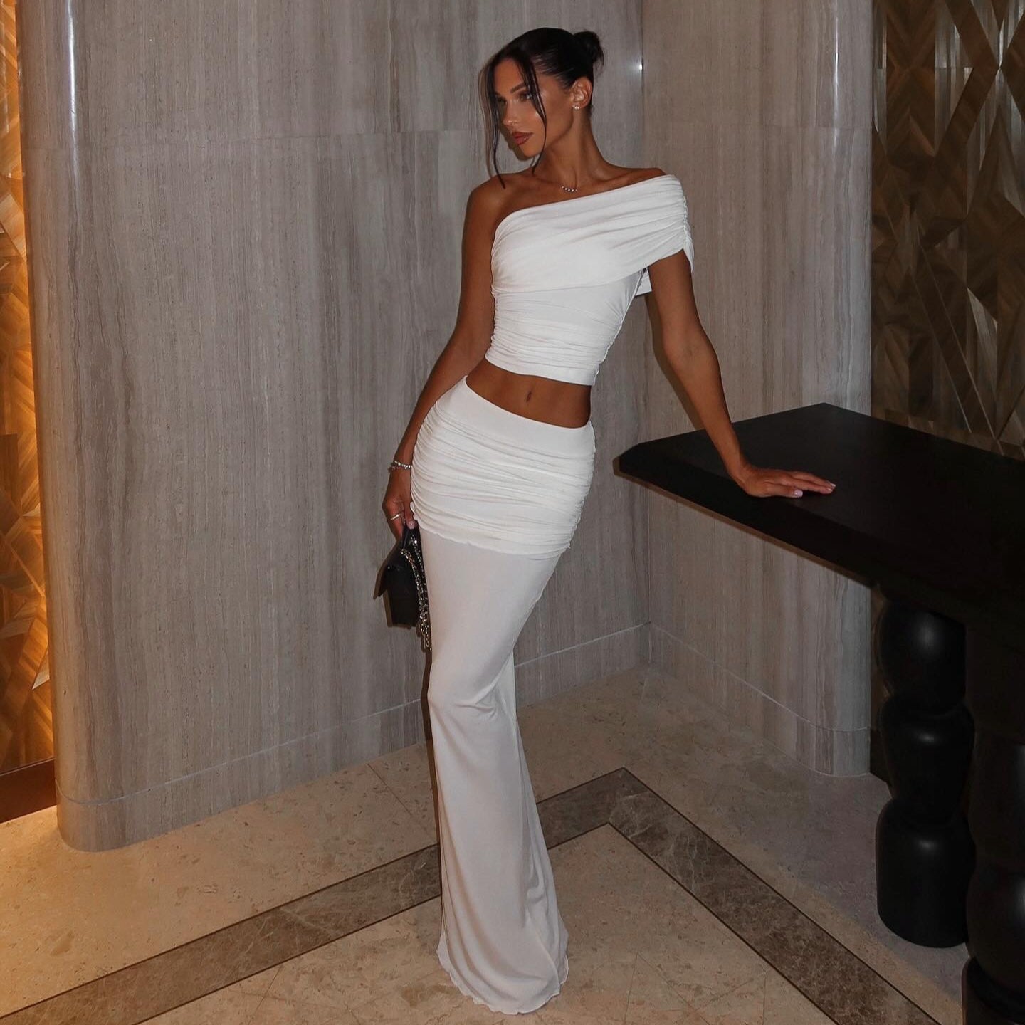 One-shoulder white two-piece set with ruched crop top and long, fitted skirt styled elegantly against a chic backdrop.