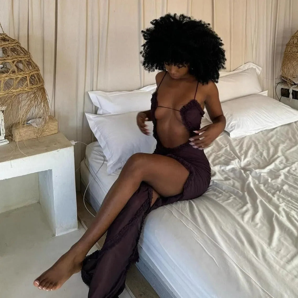 Ruched purple maxi dress with a thigh-high slit and delicate straps, styled casually while seated on a bed.