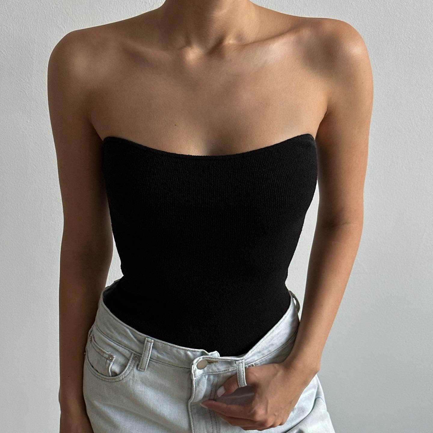 Black knitted tube top with a fitted bodice, styled with high-waisted denim for a chic summer look.
