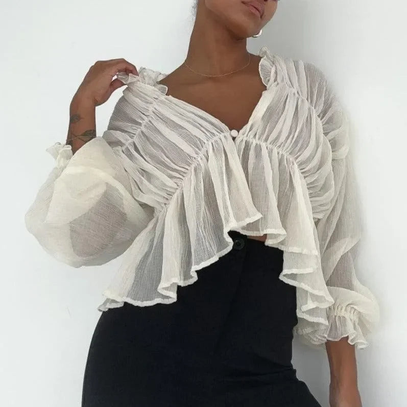 Ivory long sleeve semi-sheer top with ruffle details, styled with a high-waisted black skirt for a chic look.
