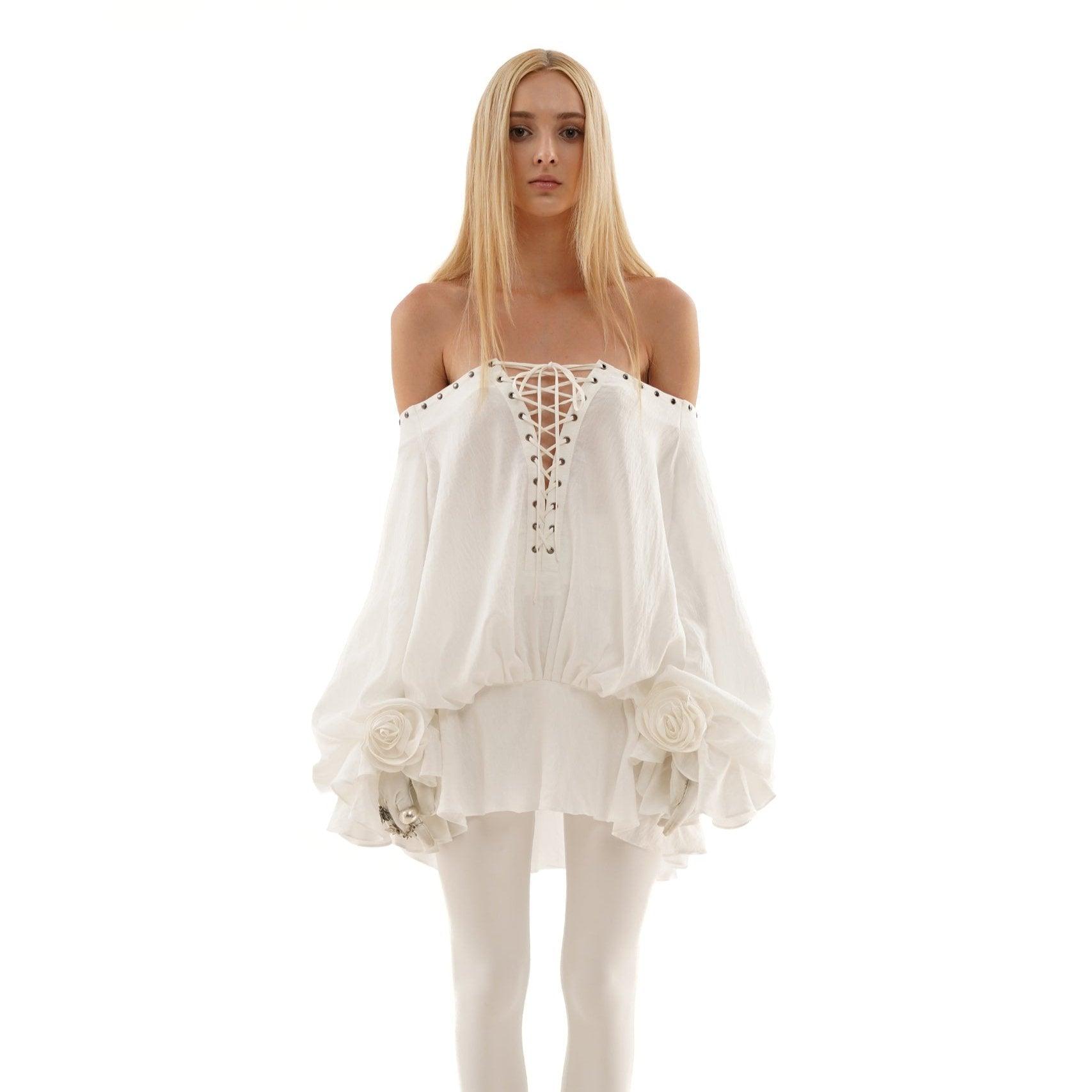 Off-shoulder white mini dress with lace-up front and balloon sleeves, styled with floral accents for a chic look.