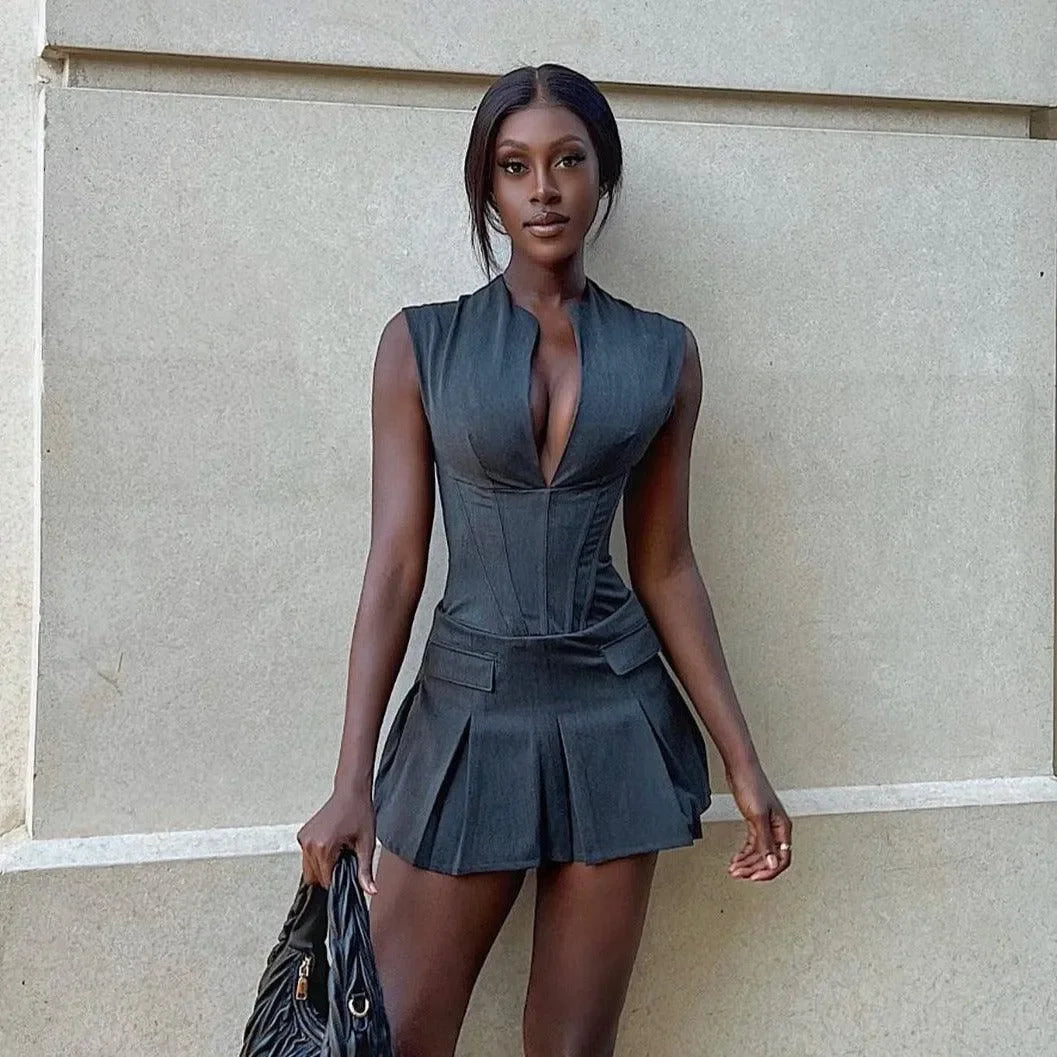 Black pleated mini dress with a corset bodice and a deep V-neck, styled effortlessly with a handbag.