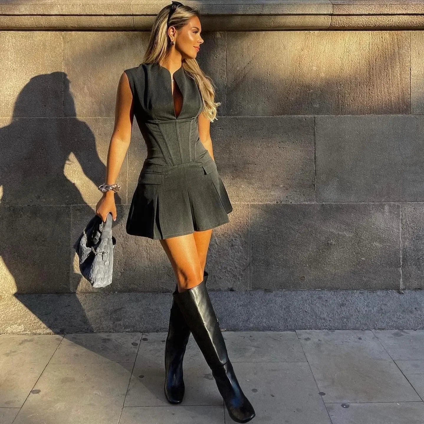 Black pleated corset mini dress with a tailored fit, styled with knee-high boots and a chic handbag. Perfect for night out.