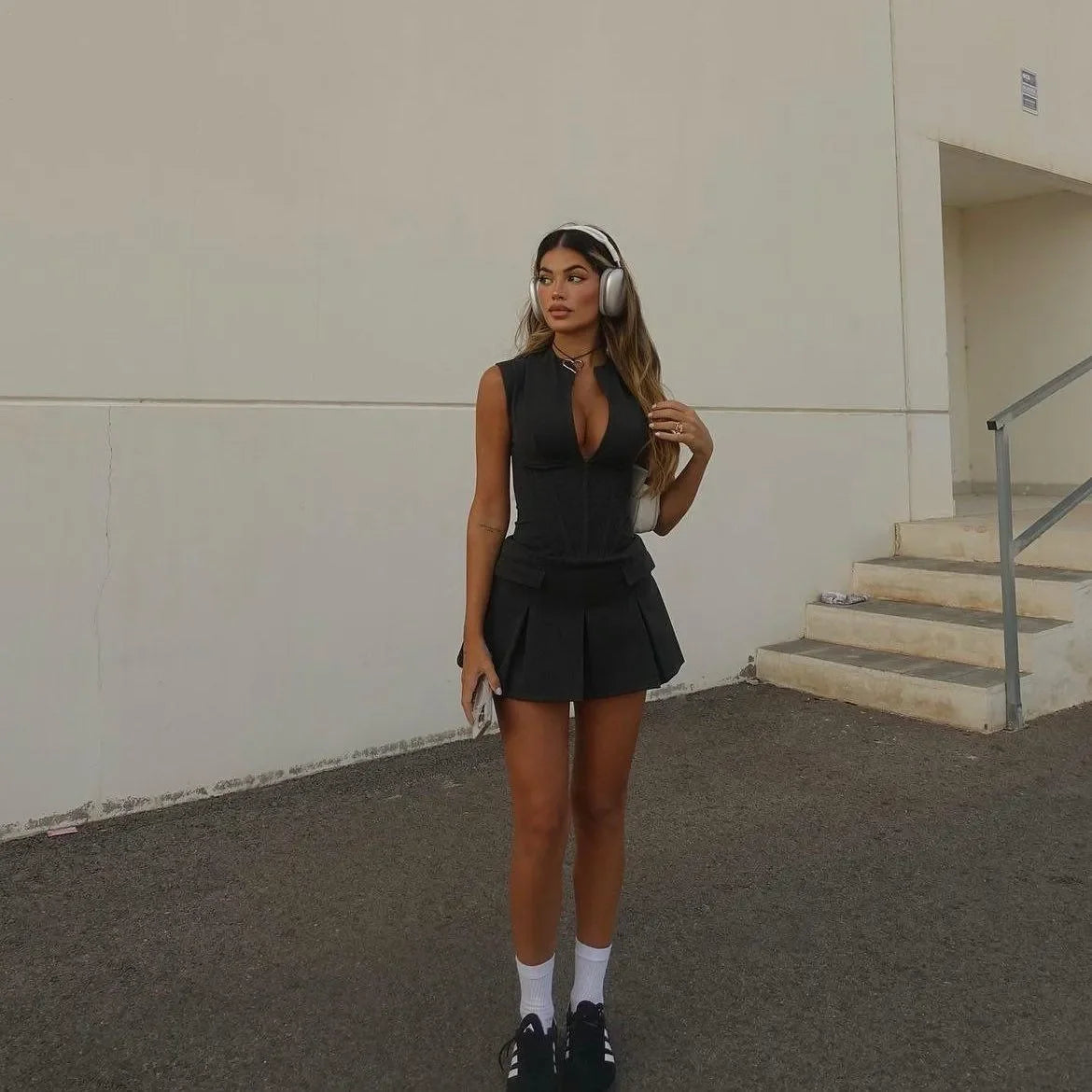 Black pleated mini dress with a corset style and deep V-neck, styled with headphones and sporty socks for a chic look.