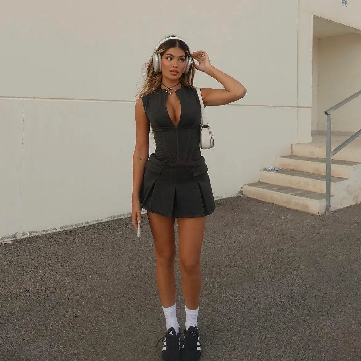 Black pleated corset mini dress with deep neckline, styled with sneakers and a choker for a chic, casual look.