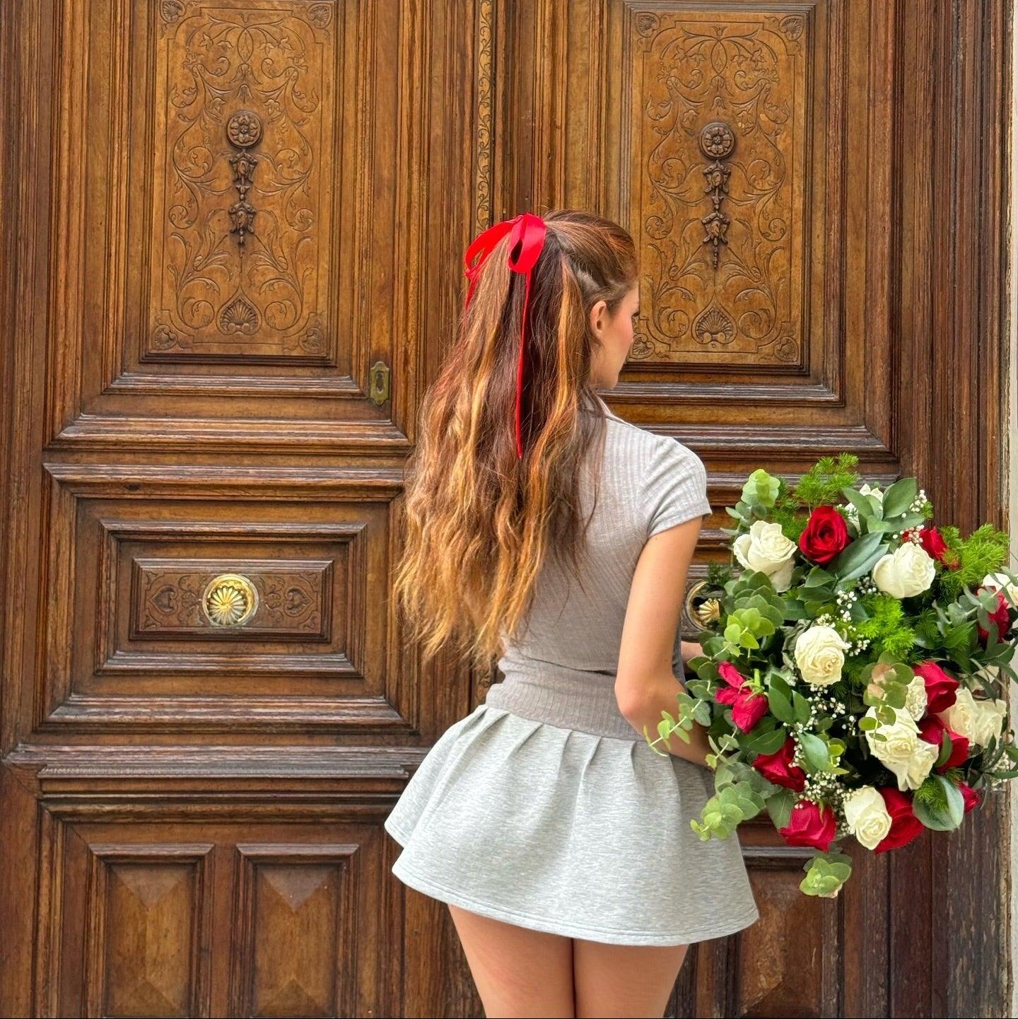 Gray polo-style knitted mini dress with a flared skirt, styled with a red ribbon in hair and holding a bouquet.