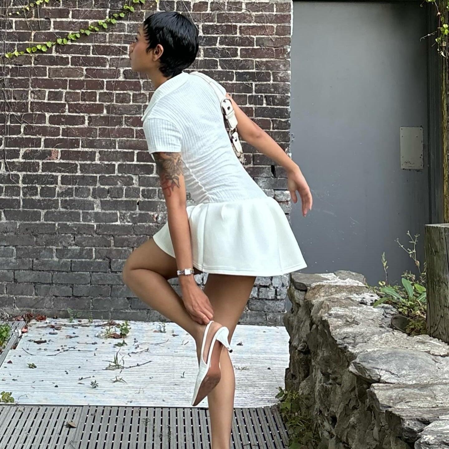 White polo-style mini dress featuring a fitted bodice and flared skirt, styled with strappy heels for a chic look.