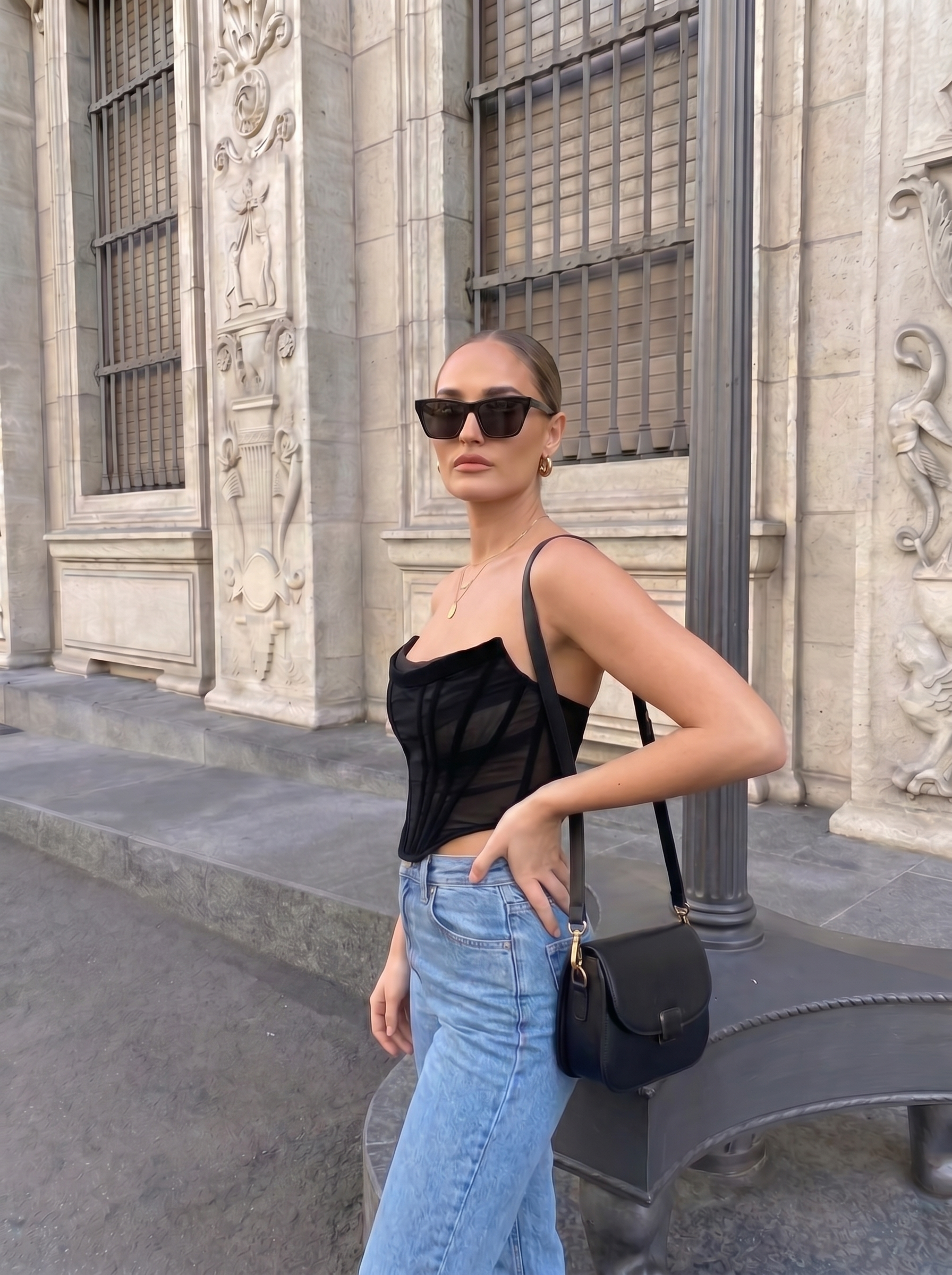 Woman in black top and blue jeans standing in front of a stone building.