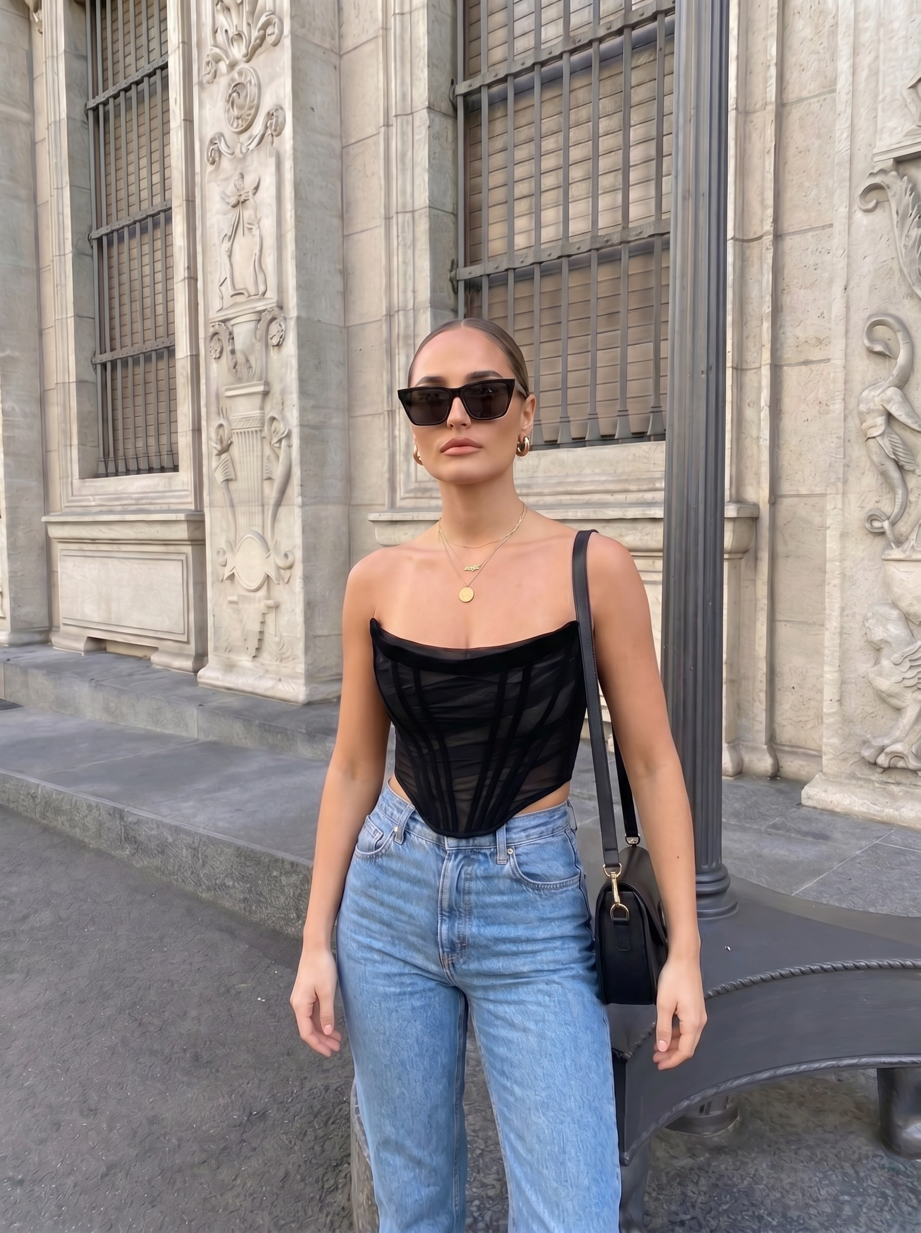 Woman wearing a black top and blue jeans standing in front of an architectural building.