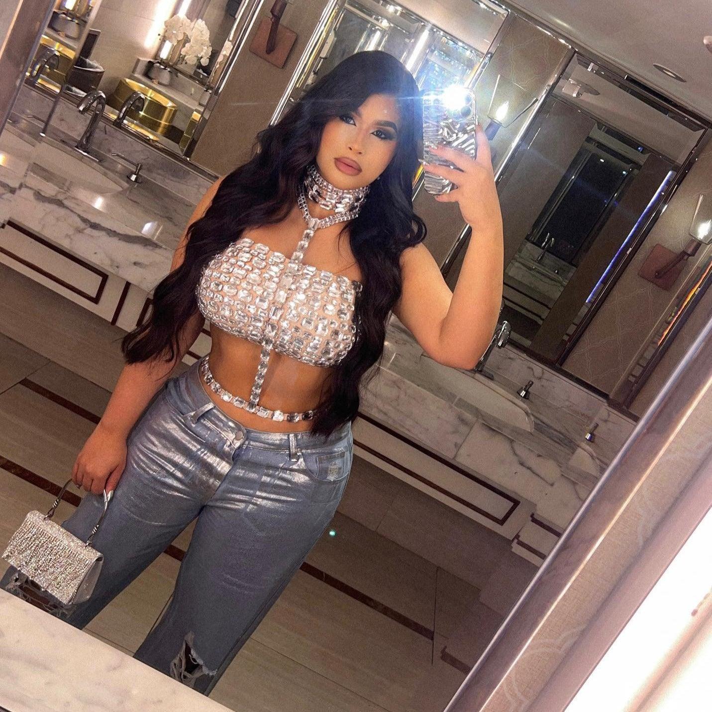 Crystal-embellished halter crop top in silver, styled with high-waisted jeans for a chic, glam look.